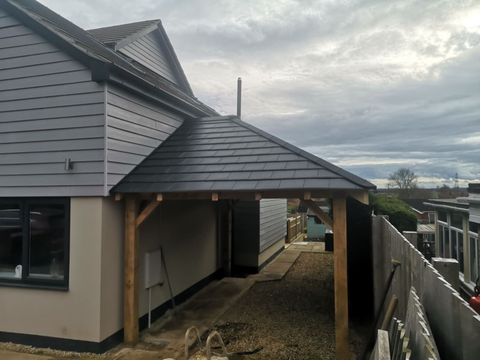 Timber-framed carport with slate roof attached to a rendered house