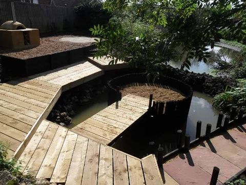 Timber decking built around a garden pond with a circular raised planter